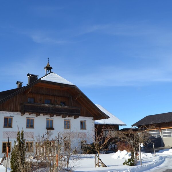 Die Außenansicht des Biobauernhofs im Winter, mit traditionellem Haupthaus und Glockentürmchen auf dem verschneiten Dach.