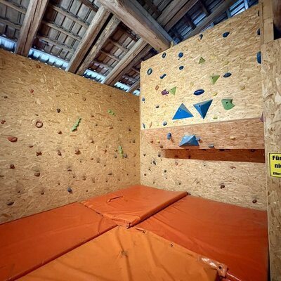 Die Boulderwand auf dem Bauernhof, ausgestattet mit bunten Griffen und Fallschutzmatten.