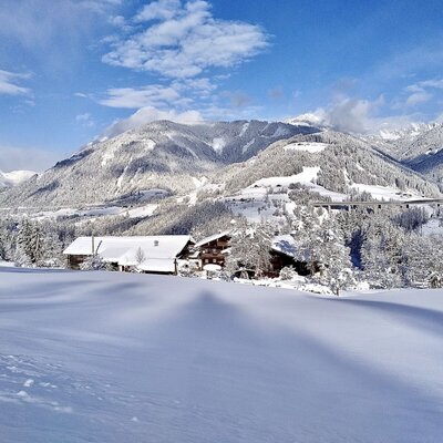 Winterlandschaft mit dem Bauernhof, schneebedeckten Bergen und Wäldern.