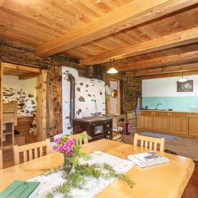 Essbereich mit Holztisch und Stühlen, einem traditionellen Ofen und einer Küche.