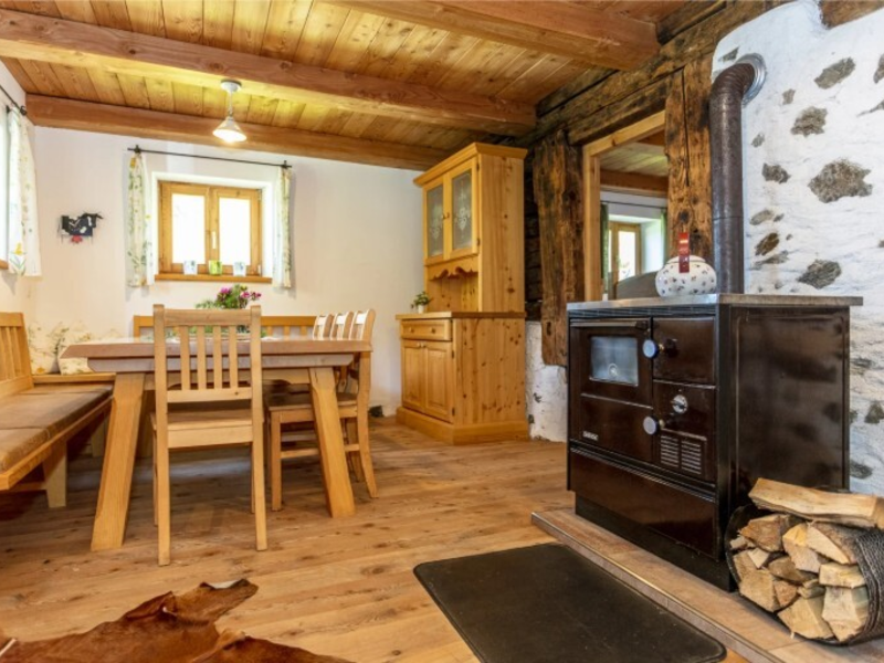 Essbereich mit Holztisch, Stühlen, Sitzbank, Holzschrank und einem Holzofen mit Brennholz.