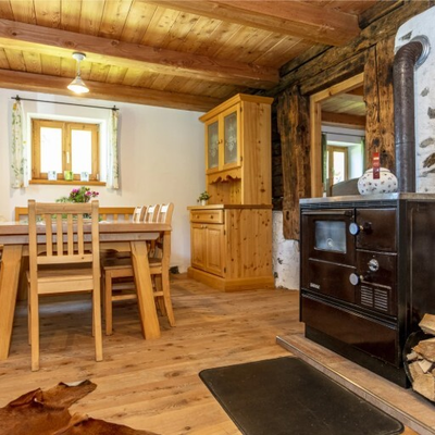Essbereich mit Holztisch, Stühlen, Sitzbank, Holzschrank und einem Holzofen mit Brennholz.