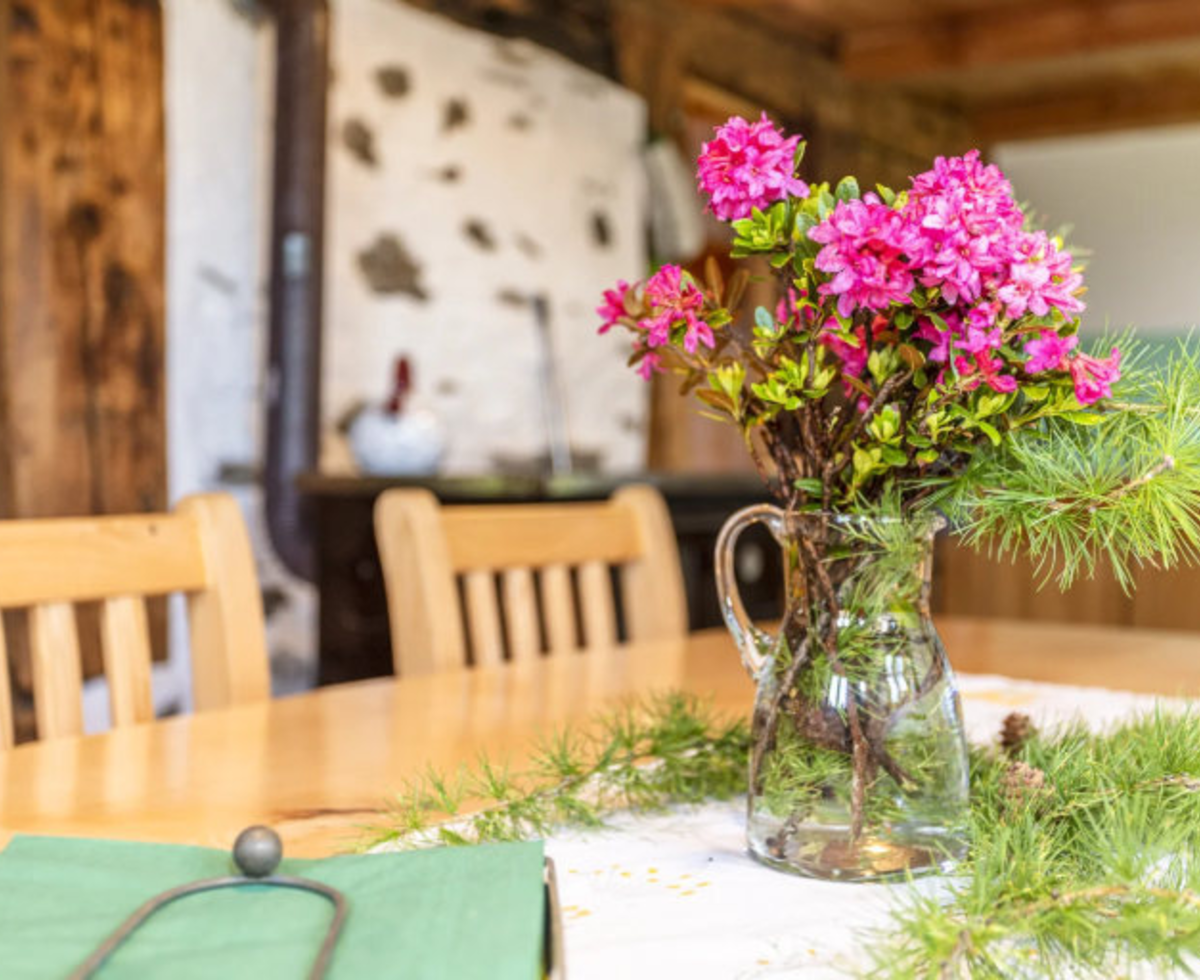 Holztisch im Essbereich, dekoriert mit rosa Blumen und Tannenzweigen, mit einem Ofen im Hintergrund.