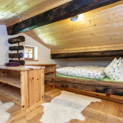 Schlafzimmer mit einem eingebauten Holzbett, Holztisch, Holzbalken und zwei Fenstern.