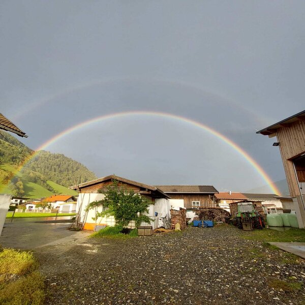 Doppelter Regenbogen über dem Hof mit Bergen im Hintergrund.
