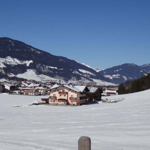 Der Bauernhof in der schneebedeckten Winterlandschaft, umgeben von Feldern und mit Blick auf die Berge.
