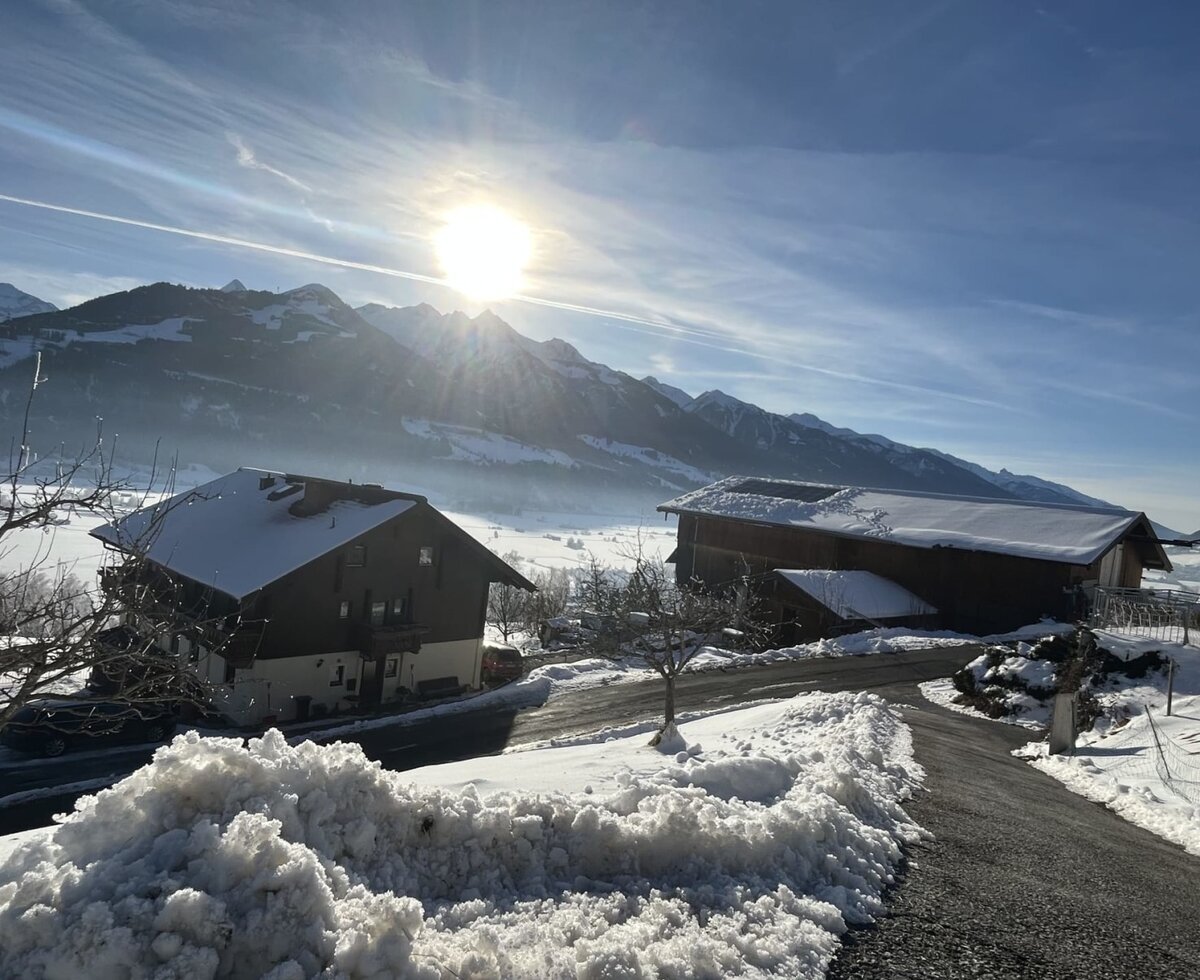 Außenansicht des Bauernhofs im Winter mit schneebedeckten Dächern und umliegender Berglandschaft.