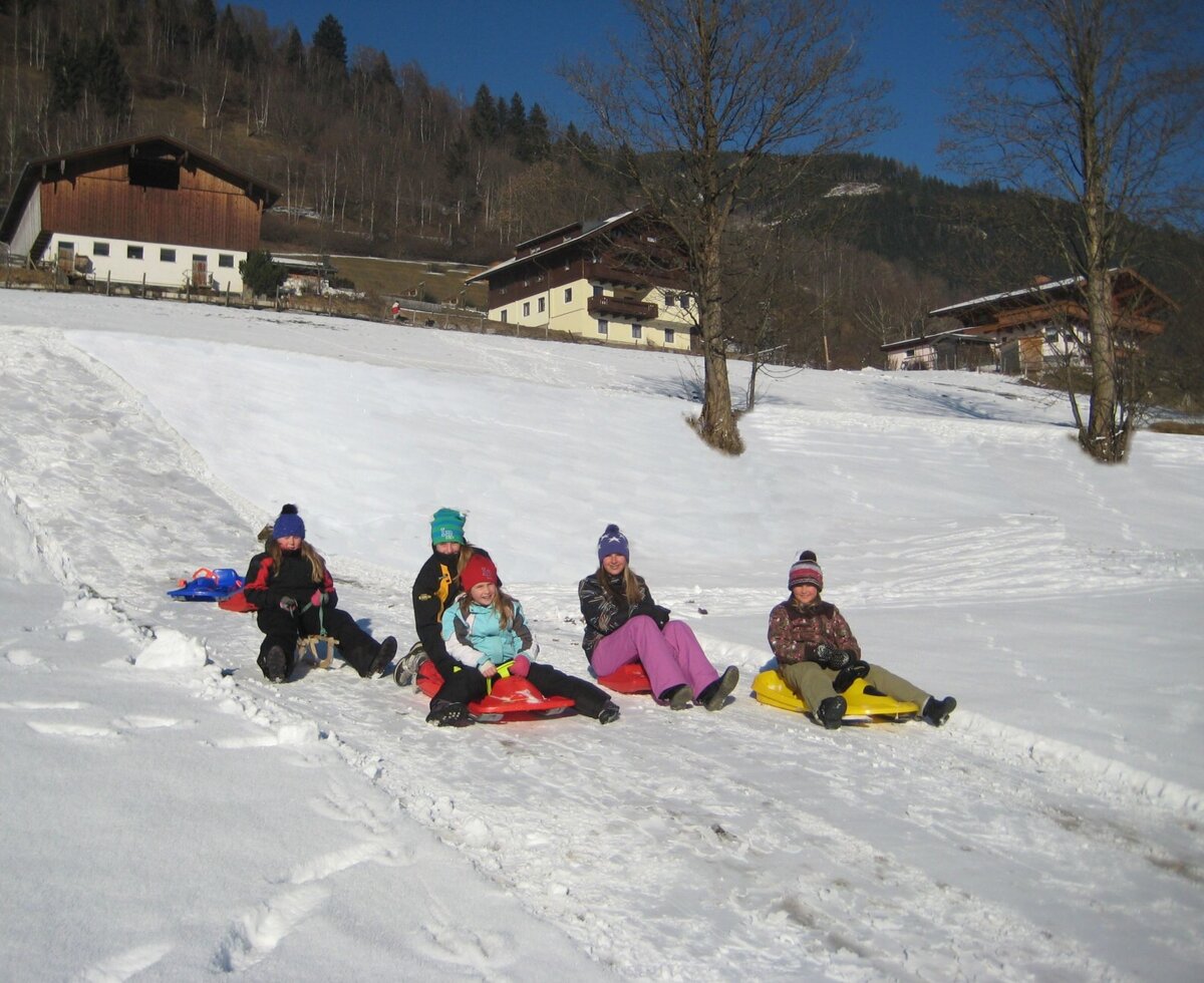 Kinder beim Rodeln im Schnee auf dem Gelände des Bauernhofs.