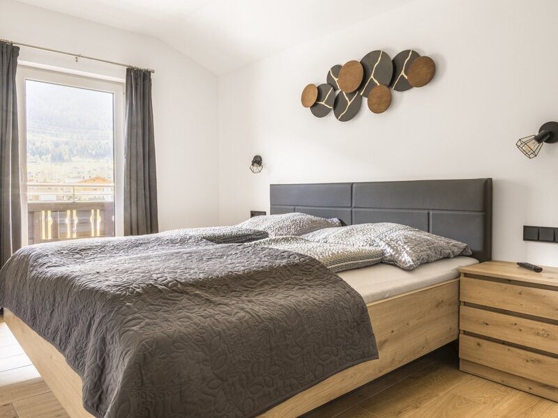 Schlafzimmer der Ferienwohnung mit Doppelbett, Holzbettrahmen, Nachttisch und Zugang zum Balkon mit Bergblick.