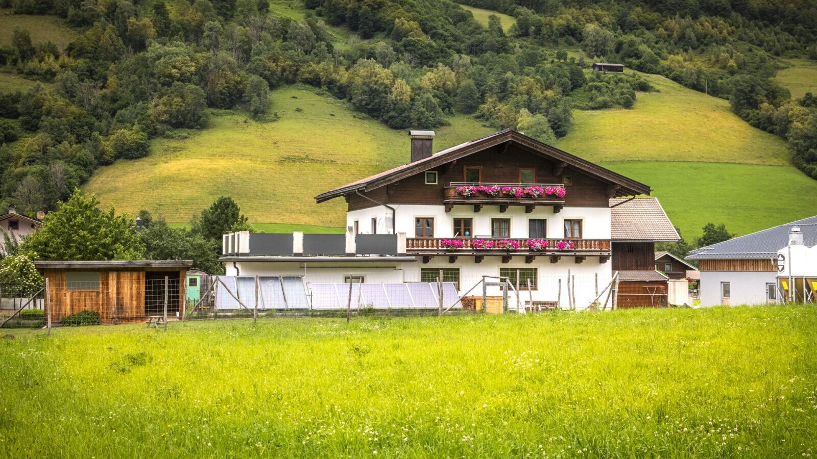 Die einladende Ferienwohnung in traditioneller Holzbauweise, umgeben von einer weitläufigen grünen Wiese vor einer bewaldeten Bergkulisse.