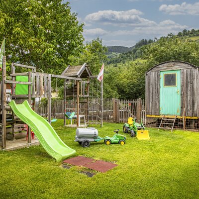 Der einladende Spielplatz der Ferienwohnung mit einer Rutsche, Spielzeugtraktoren und einer grünen Wiese.