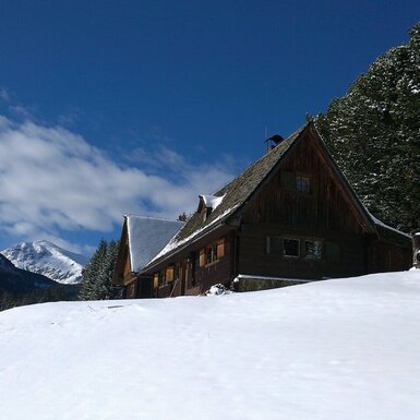 Der hölzerne Hof in einer verschneiten Berglandschaft unter blauem Himmel.