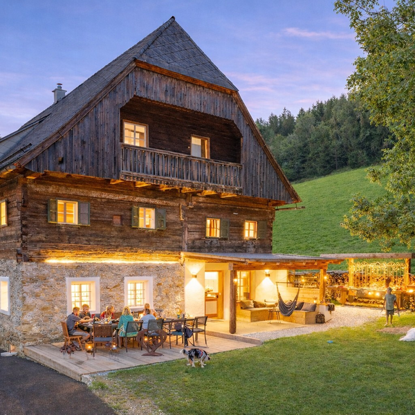 Außenansicht des Bauernhofs mit beleuchteter Terrasse, Essbereich und überdachtem Lounge-Bereich im Garten.