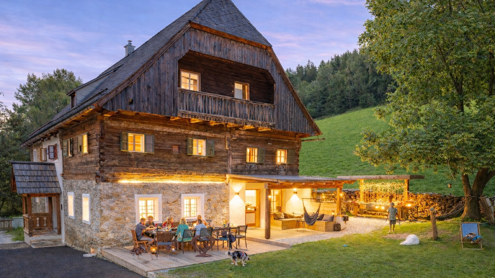 Außenansicht des Bauernhofs mit beleuchteter Terrasse, Essbereich und überdachtem Lounge-Bereich im Garten.