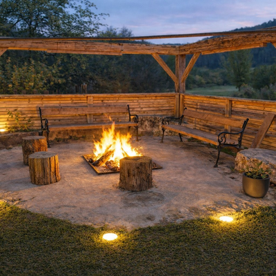 Feuerstelle mit brennendem Feuer, Holzbänken und einer Holzpergola im Außenbereich des Bauernhofs.