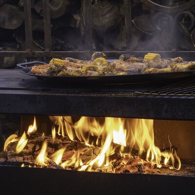 Auf dem Bauernhof werden Maiskolben und weitere Speisen auf einer Grillplatte über offenem Feuer zubereitet.