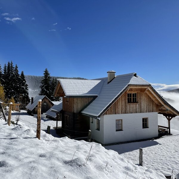 Der Hof in verschneiter Umgebung mit blauem Himmel und bewaldeter Bergkulisse.