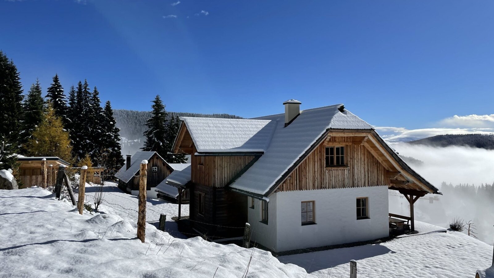 Der Hof in verschneiter Umgebung mit blauem Himmel und bewaldeter Bergkulisse.