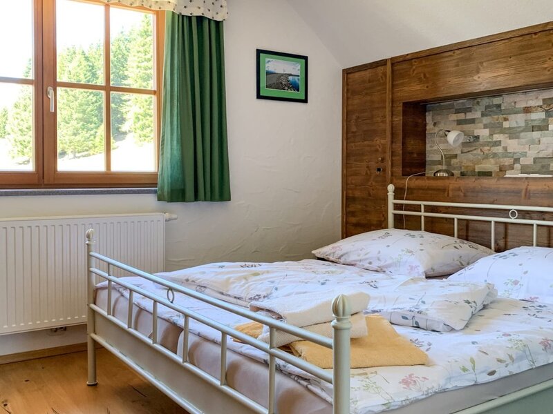 Schlafzimmer im Bed and Breakfast mit Doppelbett, Holzboden, Holzbalken und Fenster mit Blick auf Bäume.