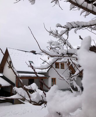 Der schneebedeckte Bauernhof im Winter, mit sichtbaren Fensterrahmen und einer überdachten Terrasse.