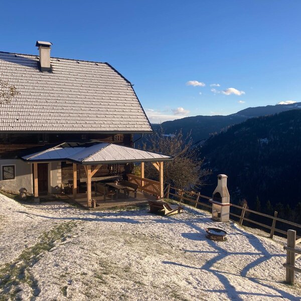 Der Hof bietet einen überdachten Außenbereich mit Esstisch, Grill und Feuerstelle, umgeben von Schnee und mit Blick auf die Berge.