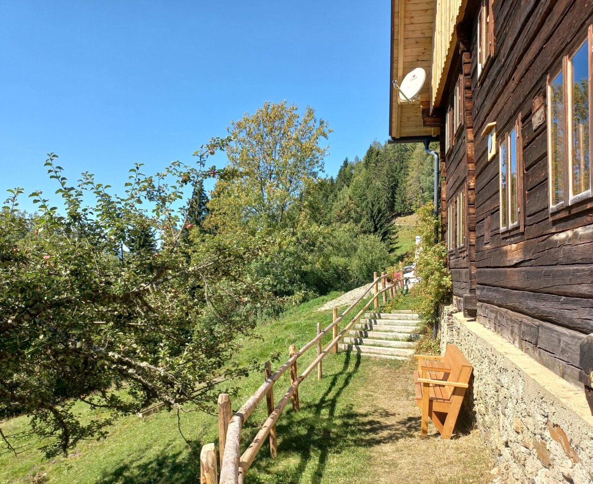 Der Hof mit traditioneller Holzfassade, einem Gartenbereich mit Apfelbaum, Treppe und einer Holzbank.