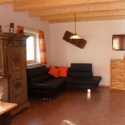 Wohnbereich im Bauernhof mit Sofa, Fernseher, traditionellem Bauernschrank und Holzbalkendecke.