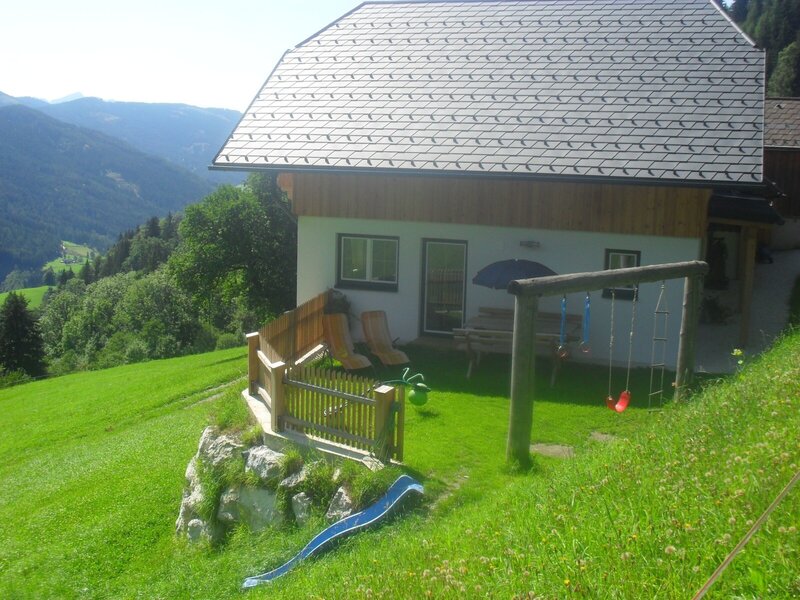 Der Garten des Bauernhofs mit Kinderspielplatz, Schaukel, Rutsche, Sonnenliegen und Bergblick.