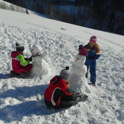 Kinder beim Schneemannbauen im Schnee auf dem Bauernhof.
