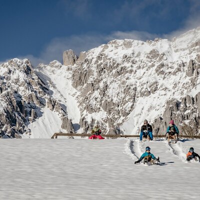 Eine winterliche Rodelpartie auf einem verschneiten Hang mit Blick auf die umliegende Berglandschaft. (c) Wolfgang Spekner