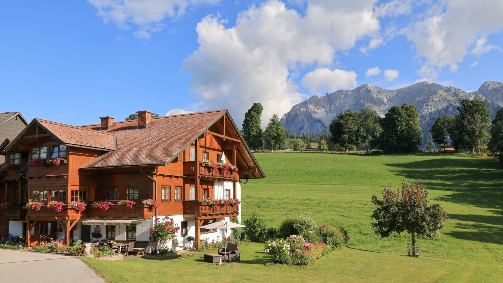 Der einladende Bauernhof mit blumengeschmückten Balkonen inmitten von grünen Wiesen vor einer malerischen Bergkulisse.