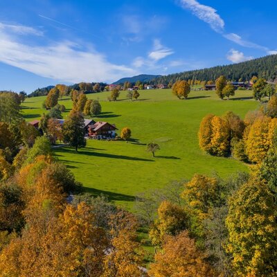Der idyllische Bauernhof eingebettet in weite grüne Wiesen und farbenfrohe Herbstwälder.