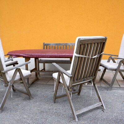 Sitzbereich im Freien des Bauernhofs mit Holztisch, Stühlen mit Auflagen und einer Holzbank.