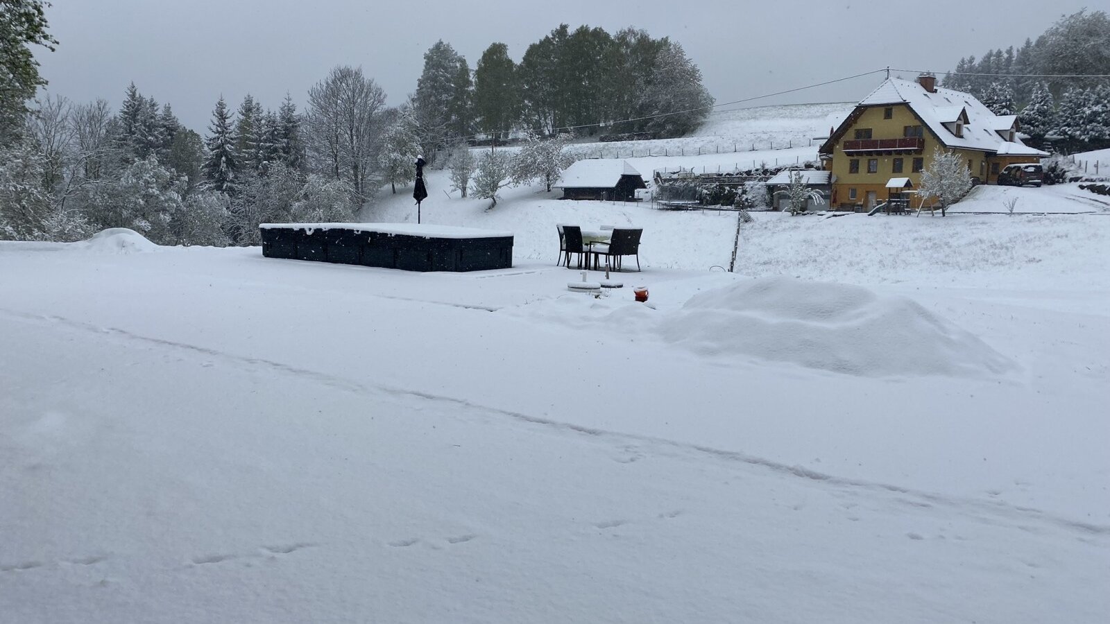 Der verschneite Außenbereich des Bauernhofs mit gelben Bauernhaus und Sitzgelegenheiten