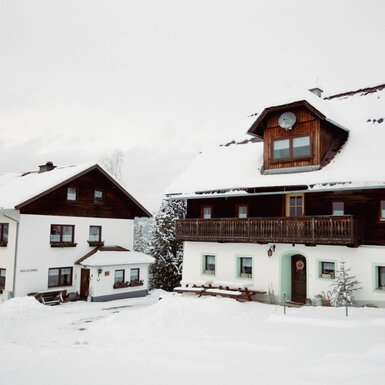 Außenansicht des Bauernhofs im Winter mit schneebedeckten Dächern und Balkonen.
