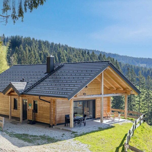 Das Blockhaus mit überdachter Terrasse und Außensitzbereich, umgeben von Wäldern und Bergen auf 1.100 m Seehöhe.