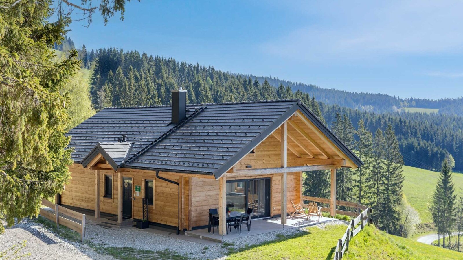Das Blockhaus mit überdachter Terrasse und Außensitzbereich, umgeben von Wäldern und Bergen auf 1.100 m Seehöhe.