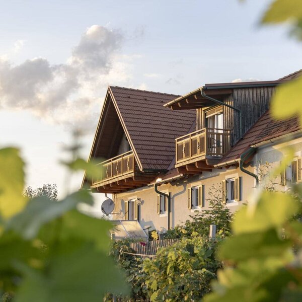 Der einladende Bauernhof mit seinen traditionellen Holzgbeln und Balkonen, sanft eingerahmt von grünen Weinreben.