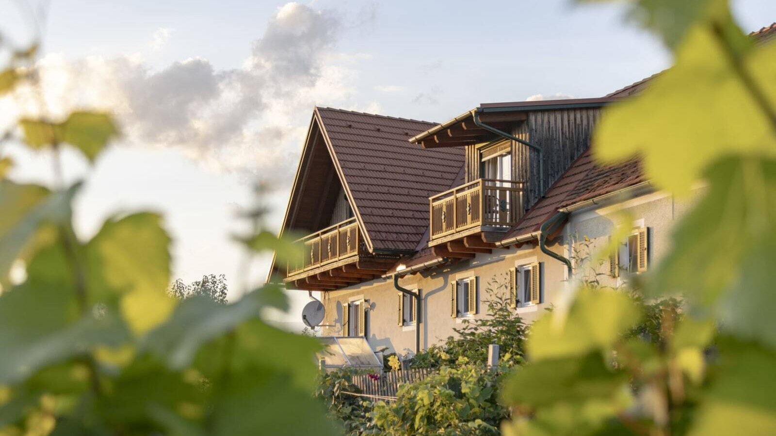 Der einladende Bauernhof mit seinen traditionellen Holzgbeln und Balkonen, sanft eingerahmt von grünen Weinreben.