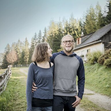 Die Außenansicht des Hofes, eingebettet in eine natürliche Landschaft mit Wald und einem Schotterweg.