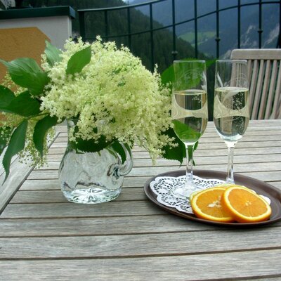 Der Balkon des Bauernhofs mit einem Holztisch, Holunderblüten, zwei Gläsern Sekt und Orangenscheiben.