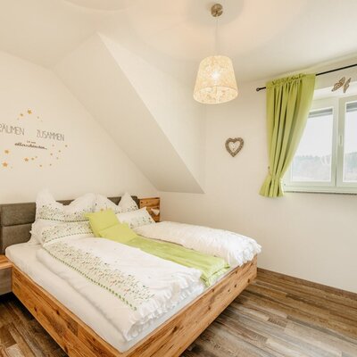 Doppelzimmer im Hof mit Holzbett, Nachttisch und einem Fenster mit hellgrünen Vorhängen.