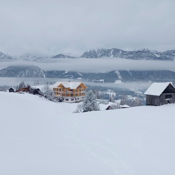 Das neue Bauernhaus in einer verschneiten Winterlandschaft mit Bergen im Hintergrund.