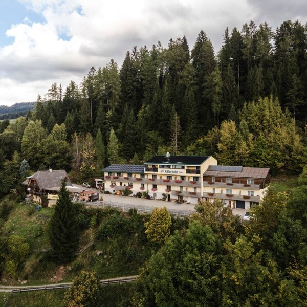 Außenansicht des Bauernhofs Käferhube, bestehend aus mehreren Gebäuden, eingebettet in eine bewaldete Berglandschaft.