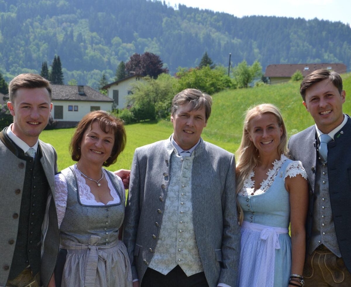 Die Gastgeberfamilie des Bauernhofs in traditioneller Kleidung vor der Berglandschaft.