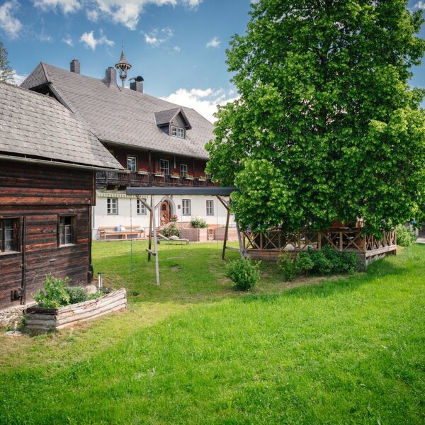Der Bauernhof mit einem traditionellen Holzgebäude, einem großen Garten mit Schaukel und einem Baum mit Sitzbereich.