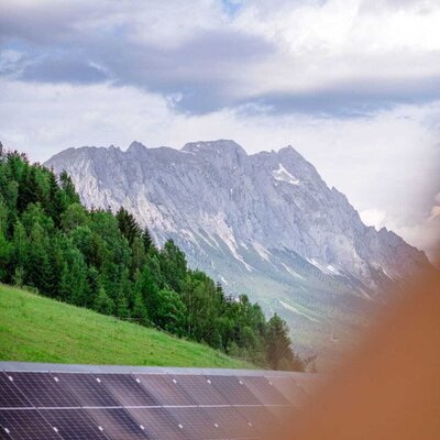Solarpaneele auf dem Dach des Bauernhofs mit Blick auf die Berge und eine bewaldete Anhöhe.