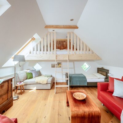 Dachzimmer im Bauernhof mit einem Hochbett, einem Einzelbett und einem Wohnbereich mit zwei Sofas.