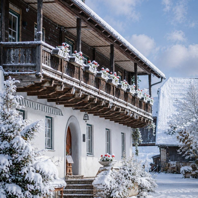 Ein einladender, winterlich verschneiter Bauernhof mit traditionellem Holzbalkon unter blauem Himmel.