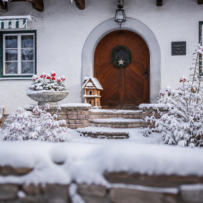 Der einladende, schneebedeckte Eingangsbereich des Bauernhofs mit einer rustikalen Holztür und festlicher Dekoration.